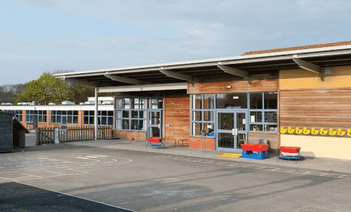 Modern primary school playground with outdoor toys, large windows, and wooden exterior on a sunny day.