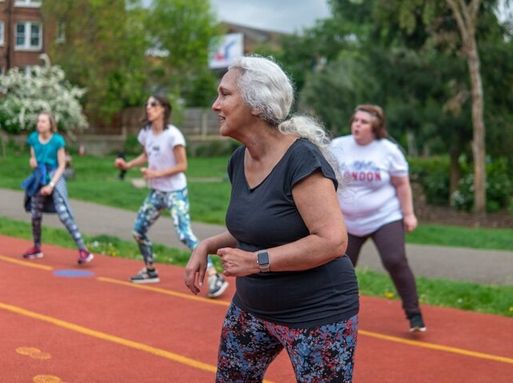 An elderly white woman exercises in a park with others